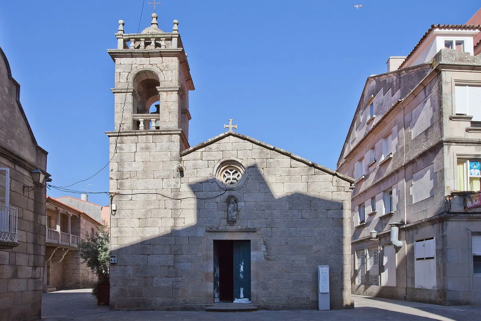 La antigua iglesia parroquial de San Xes de Padriñán, de piedra, con su torre y la plaza delante