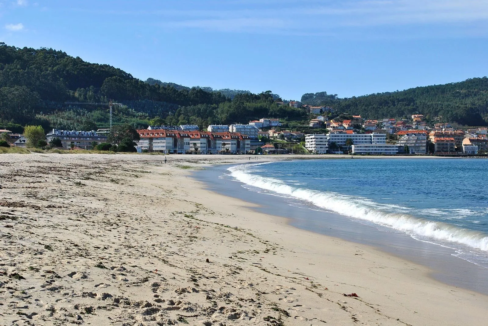 Playa de Ladeira con olas suaves y las casas de Baiona al fondo