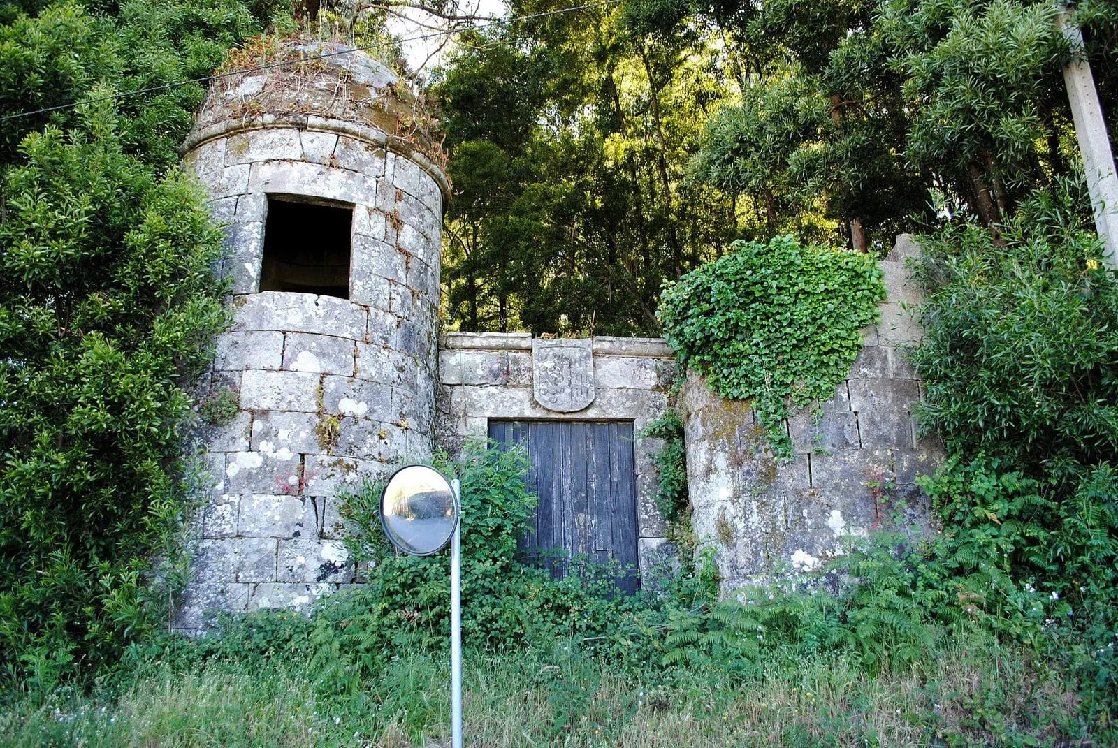 Garita circular y puerta de madera entre muros de piedra cubiertos de hiedra en el pazo del Conde de Gondomar