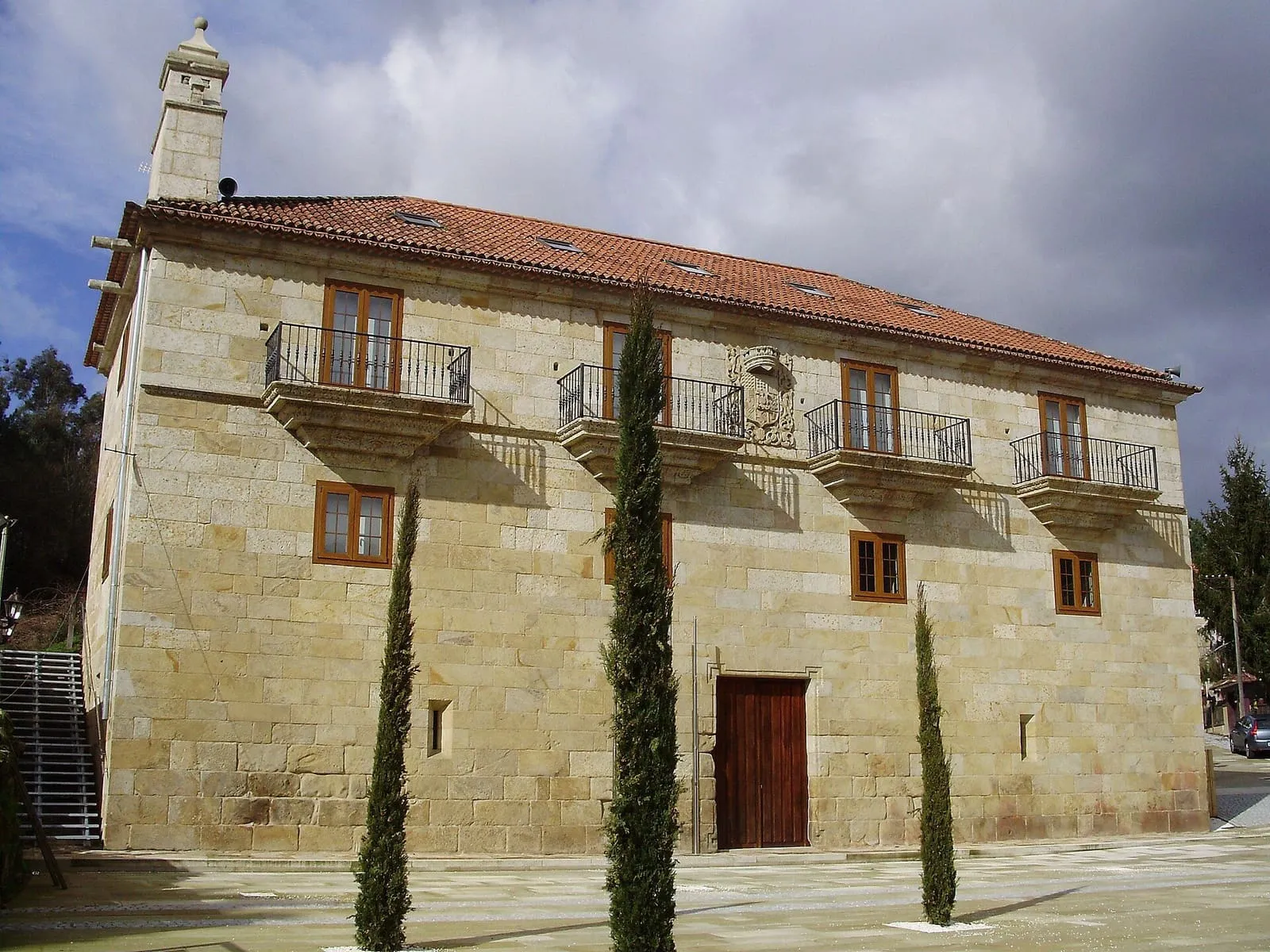 Fachada de piedra del Pazo de Mos, con cipreses delante y el cielo al fondo