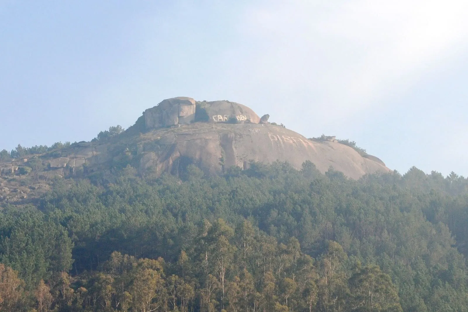 El peñasco del Castelo de Cans, sobre un bosque de pinos, junto a la ruta de los molinos