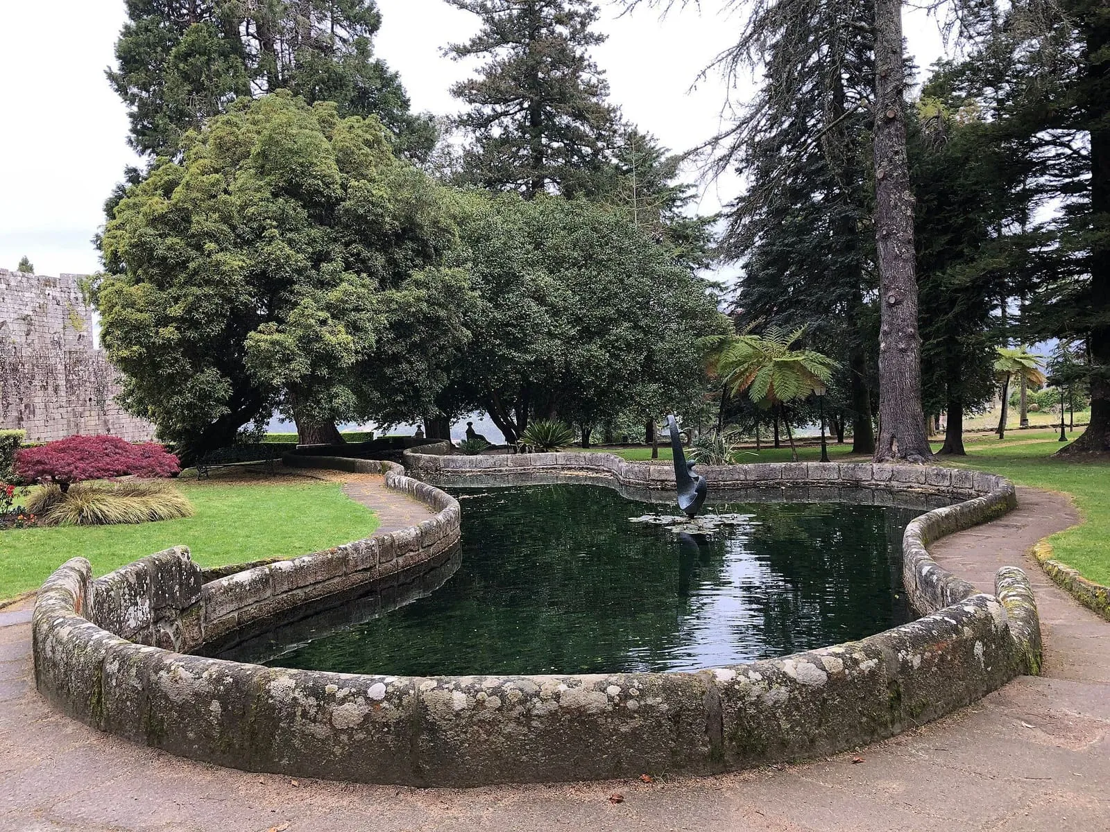 El estanque de borde de piedra en los jardines del castillo de Soutomaior, rodeado de césped y árboles